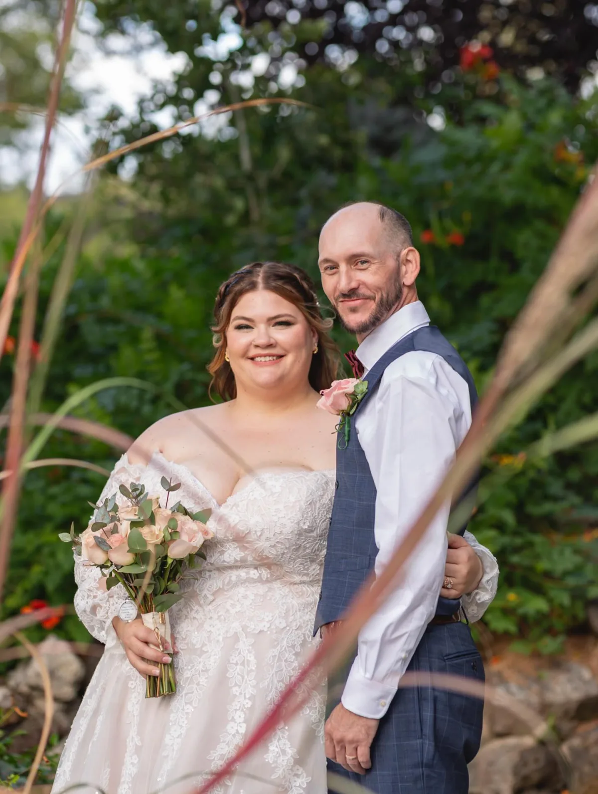 Bride holding a blush rose bouquet standing with her groom in a green Colorado garden