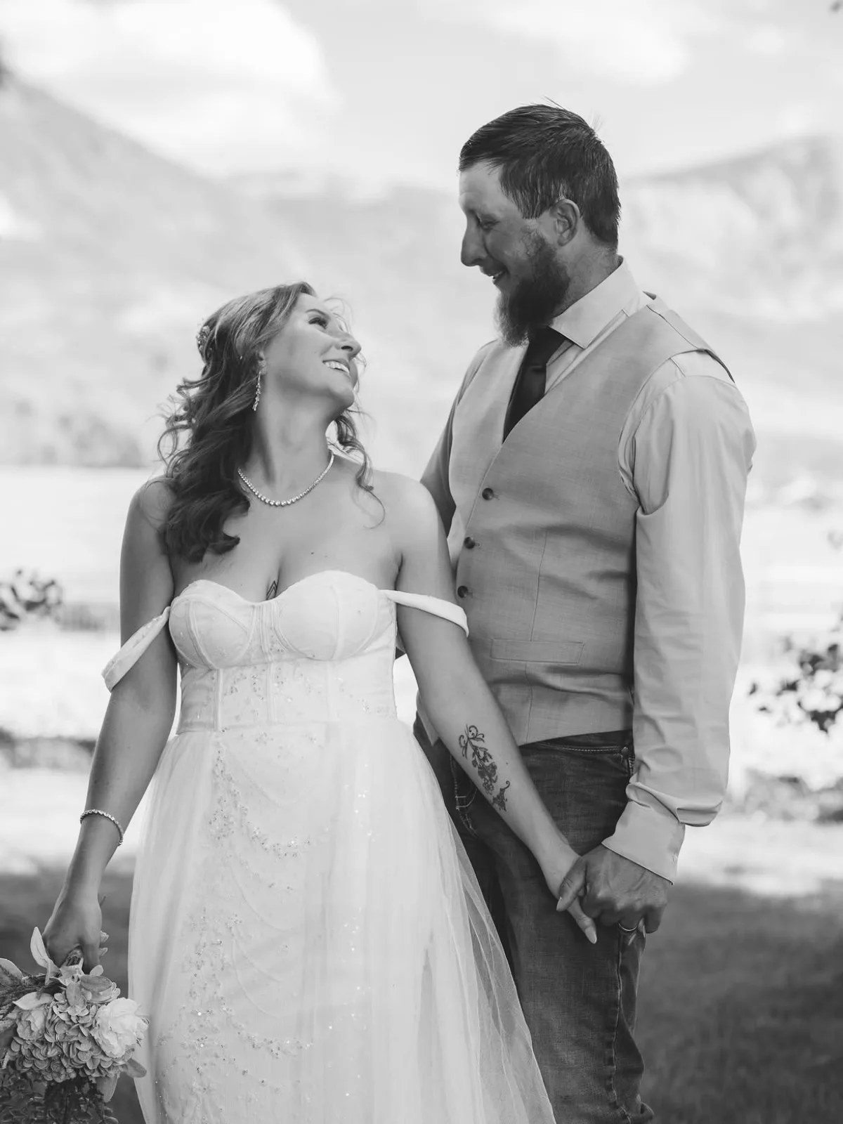 Black and white photo of a bride looking up at her groom with Colorado mountains behind them