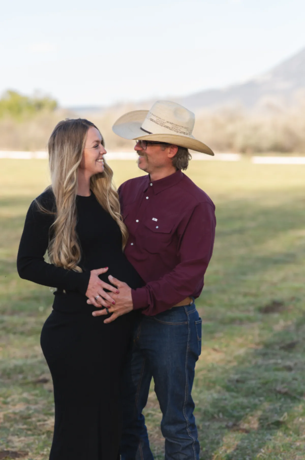 Expecting couple laughing together in a green pasture with a mesa behind them