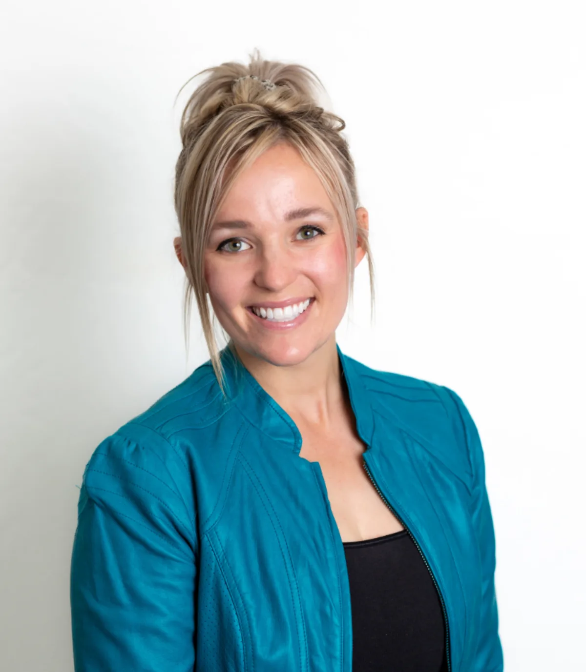 Woman in a teal jacket smiling against a clean white studio background