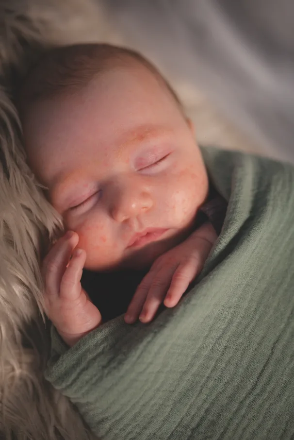 Close up of a newborn sleeping in a sage green muslin wrap on soft fur