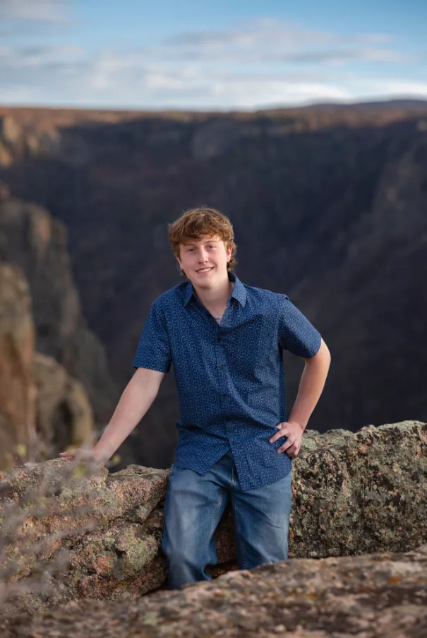 Senior portrait of a young man seated on a rock ledge above the Black Canyon