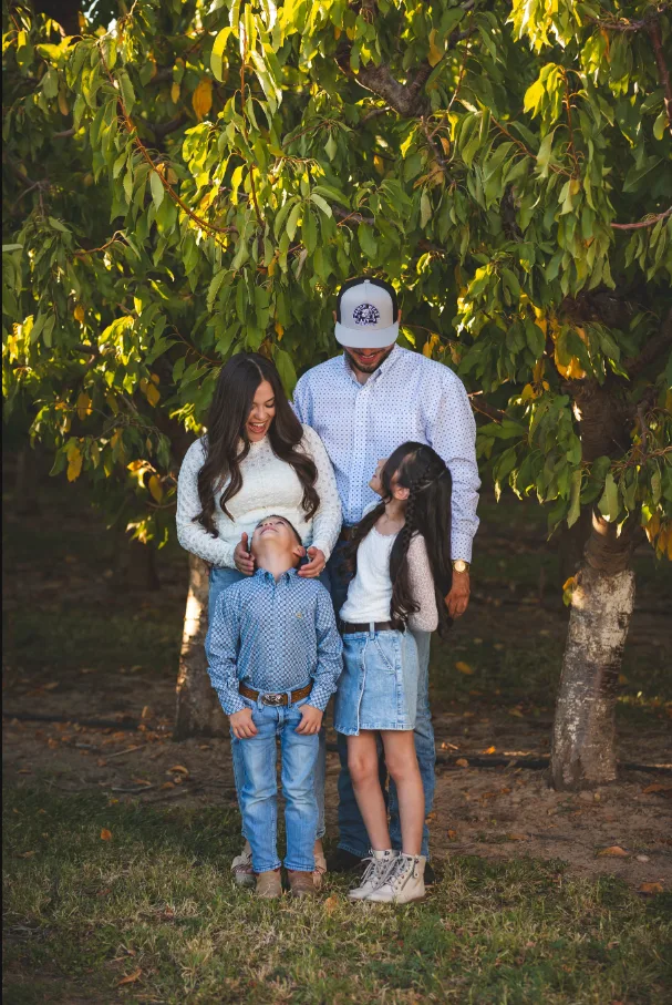 Family of four laughing beneath a fruit tree in a Colorado orchard