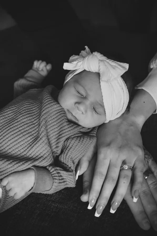 Black and white photo of a sleeping newborn in a knit sweater resting on her mother's hand