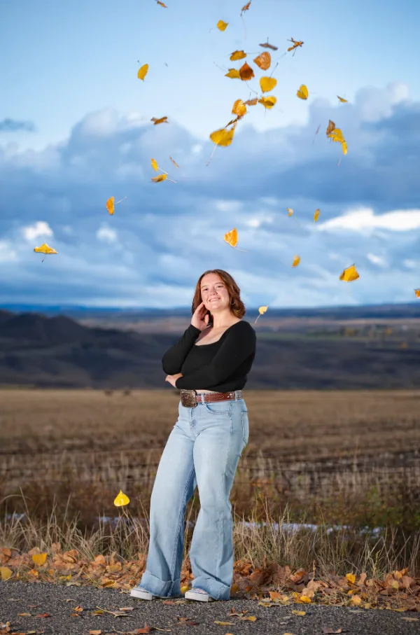 Senior girl laughing as autumn cottonwood leaves fall around her on a Colorado road