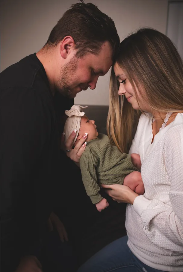 New parents leaning together forehead to forehead while holding their newborn daughter