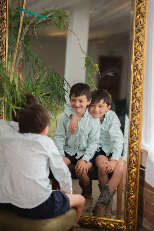 Two brothers in matching shirts reflected in an ornate gold mirror indoors
