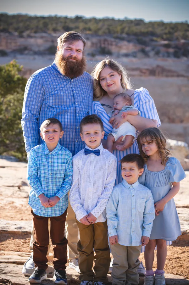 Family of seven with a newborn standing together on a sunlit Colorado mesa rim