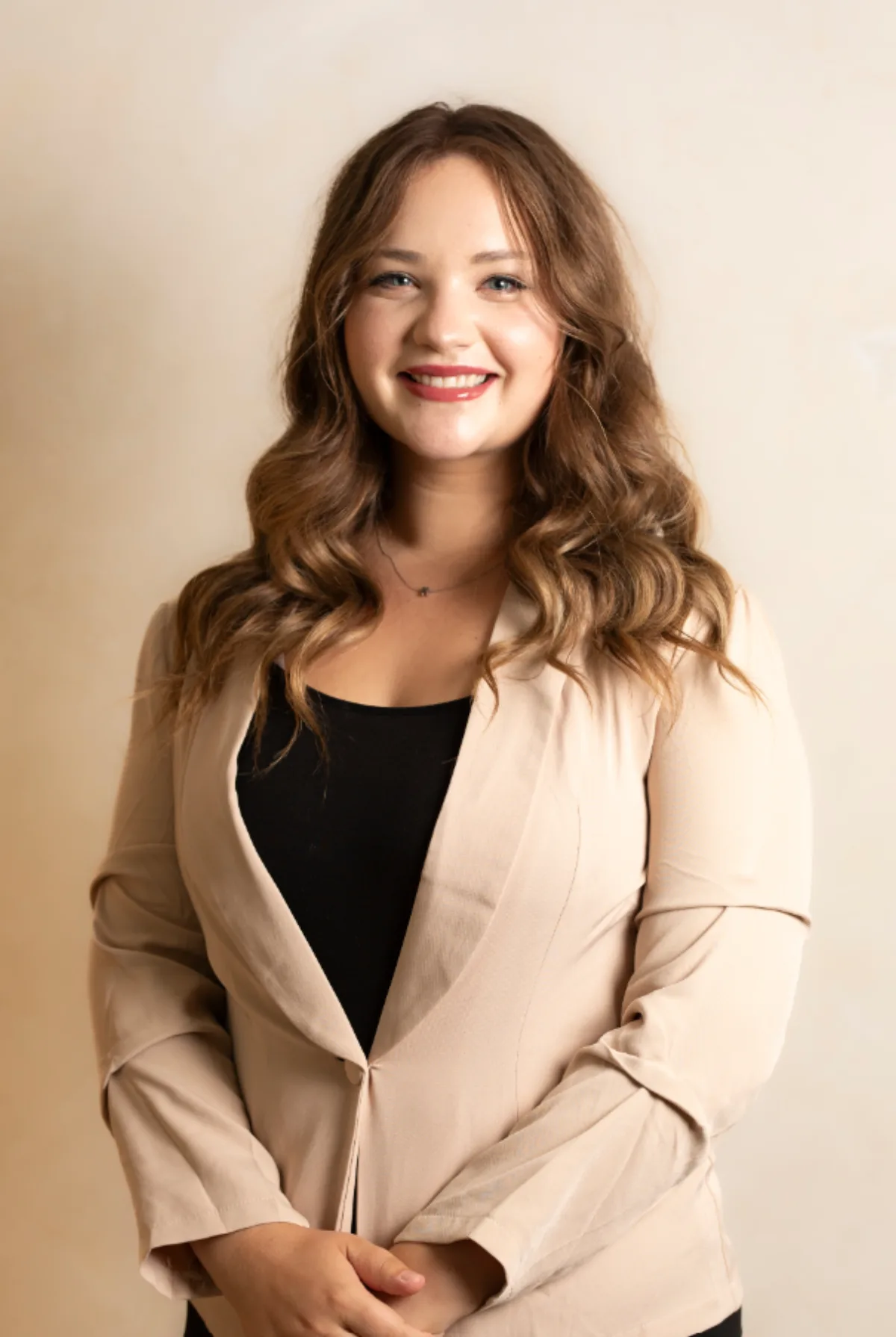 Smiling woman in a tan blazer photographed against a warm cream backdrop