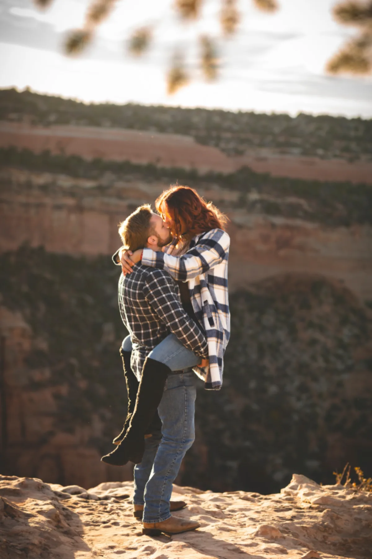 Engaged couple kissing as he lifts her at the edge of a sunlit Colorado canyon